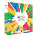 Decorum board game box featuring a colorful geometric design with painted room interiors arranged in a radial pattern around a white center circle. The box displays the game title "décorum" prominently in the center with the tagline "A game of passive aggressive cohabitation" underneath.