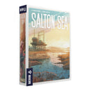 alton Sea board game box showing an industrial geothermal facility with drilling equipment and smokestacks situated beside a reflective body of water at sunset. The cover art features warm golden and teal tones with the facility reflected in the calm water, while rocky shoreline and distant mountains frame the scene.