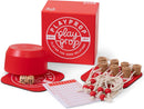 PlayProp board game set displaying red packaging box with circular logo and tagline 'Playing for Good Relations Since 1977'. The game components are arranged around the box including wooden dice, cork game pieces with strings attached, red wooden tokens, score sheets, and a red circular game board or mat. The entire set features a cohesive red and white color scheme with natural wood accents.