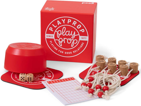 PlayProp board game set displaying red packaging box with circular logo and tagline 'Playing for Good Relations Since 1977'. The game components are arranged around the box including wooden dice, cork game pieces with strings attached, red wooden tokens, score sheets, and a red circular game board or mat. The entire set features a cohesive red and white color scheme with natural wood accents.