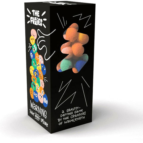 The Fuzzies board game box featuring a black package with colorful fuzzy balls stacked in a gravity-defying tower on the front panel. The left side shows cartoon-style emoji faces in various colors with "THE FUZZIES" branding and a "WARNING" label, while the right side displays the stacked fuzzy balls with radiating lines suggesting movement or impact. 