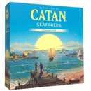Box cover of Catan Seafarers Expansion showing a coastal scene with sailing ships on blue waters and a large setting sun on the horizon. The artwork depicts wooden docks, small coastal settlements, and multiple ships with billowing sails navigating between islands.