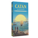 Box of Catan Seafarers 5-6 Player Expansion, featuring a blue box with the Catan logo in yellow and several sailing ships on a blue ocean. The box cover artwork shows people watching from a wooden dock as ships with white sails navigate the waters, with a large sun setting on the horizon.
