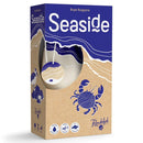 Seaside board game box by Bryan Burgoyne published by Randolph, featuring an artistic blue and tan design with layered wave patterns and a stylized crab illustration on sandy beach colors. The box has a distinctive oval window cutout on the front that reveals wooden game tokens inside. 