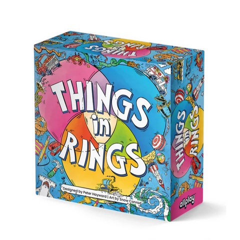 Things in Rings board game box featuring a colorful, cartoon-style design with the game title displayed in large white letters across overlapping pink, blue, and yellow circles. The box art includes whimsical illustrations of various objects, characters, and symbols scattered across a bright blue background in a playful, hand-drawn style.