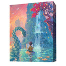 Canvas board game box cover featuring a whimsical painted scene of a young artist sitting by a tranquil blue waterfall in a fantastical landscape. The artwork displays vibrant colors with a pink and orange sunset sky, floating geometric shapes, lily pads on the water, and a large serpentine creature made of teal and green segments arching through the scene. 