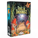 Box art for Toil & Troublez, featuring a large toad surrounded by red mushrooms and magical elements against a dark fantasy background. Two silhouetted witch figures face each other with wands in the center, with the tagline "FIND THE MAGIC. IF YOU DARE." 